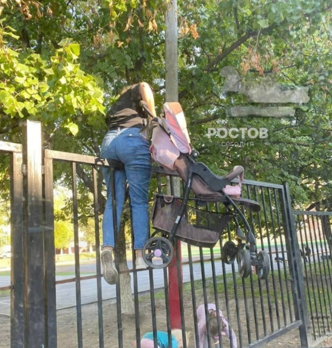 Жительница Ростова решила не обходить забор вокруг школы №30 на Северном. Молодая мама перелезла через него с двумя детьми и коляской. 